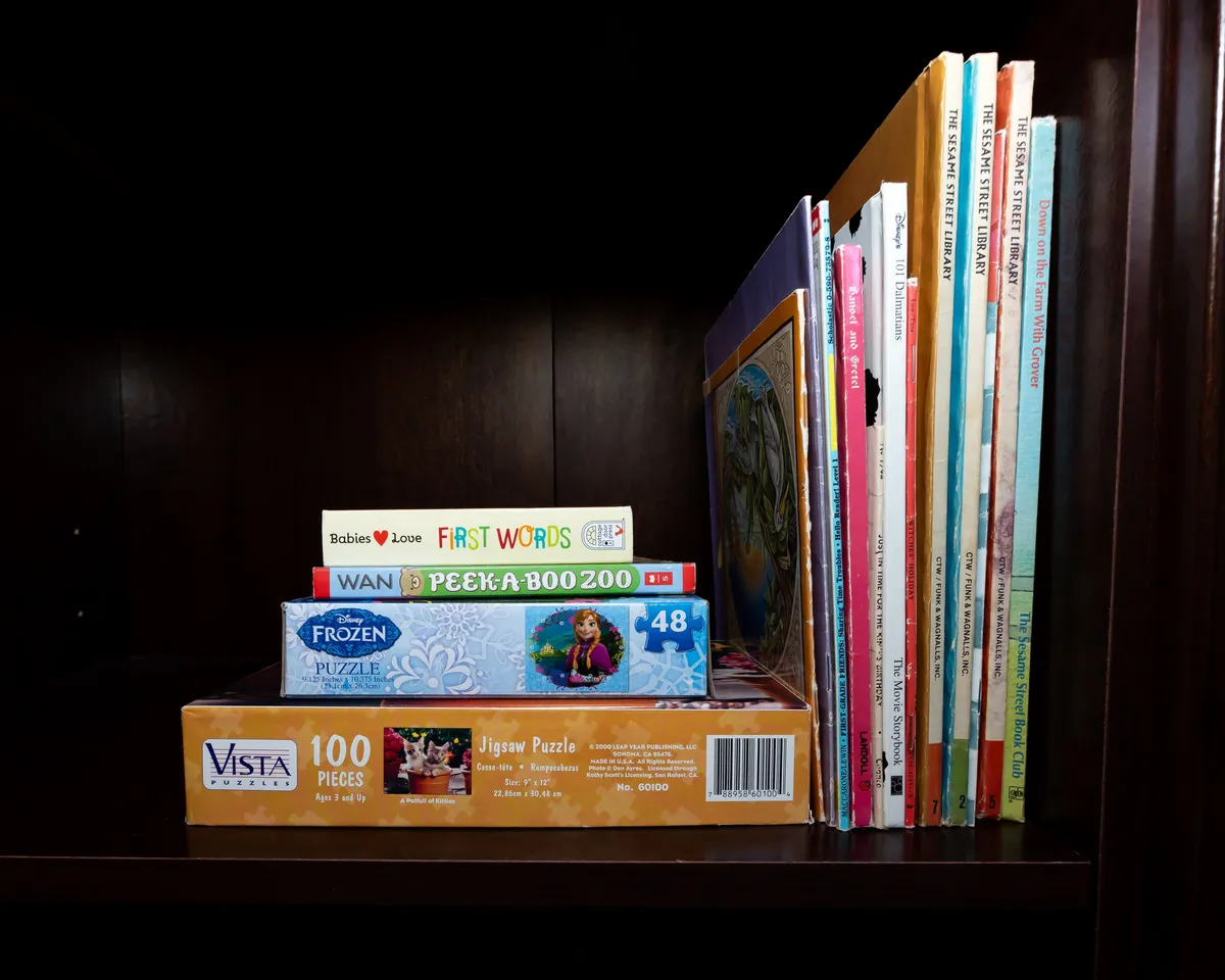 A cozy nook featuring a selection of children's books and jigsaw puzzles, creating a family-friendly corner ideal for little ones and their caregivers. The space feels inviting and nostalgic, emphasizing comfort and interactive play.