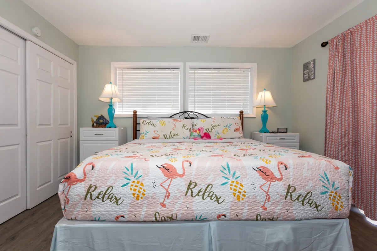 A bedroom featuring a bed with a colorful quilt, flanked by nightstands with lamps and soft curtains drawn for privacy. The arrangement looks inviting and is suitable for families, couples, or friends seeking a restful space.