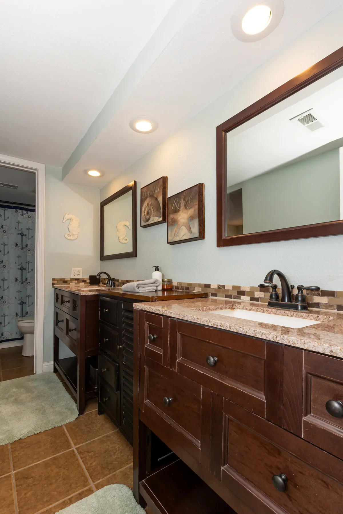 A bright, tranquil bathroom with a dual-sink vanity, large framed mirrors, decorative wall art, and a textured countertop, creating a spa-like environment ideal for morning routines and evening relaxation.