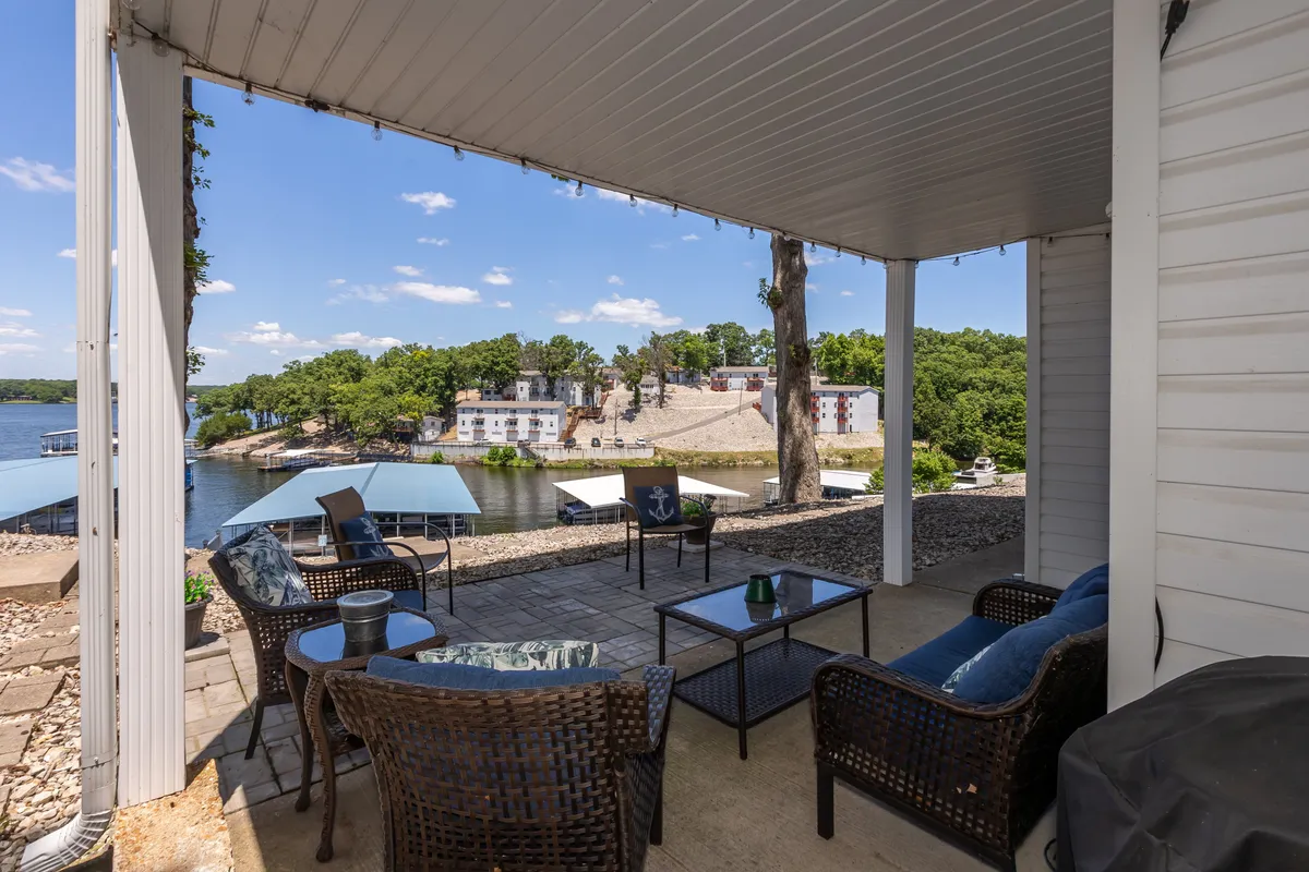This exterior image captures a tranquil waterfront scene, featuring an inviting outdoor seating area and a private dock extending into the lake. The area feels serene and perfect for relaxing, socializing, or enjoying time with pets in the fresh air. The presence of outdoor furniture suggests a pet-friendly patio where guests can unwind with their furry companions.