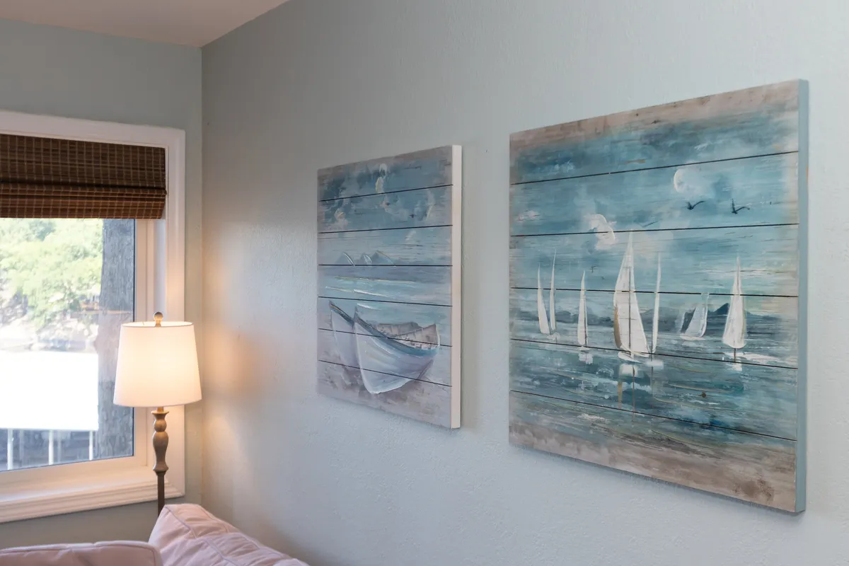 A serene interior featuring paintings of boats and sailboats, a lamp, and a window that offers a view outside. The room is calm and tastefully decorated with a nautical theme, reinforcing the boating and lake lifestyle.
