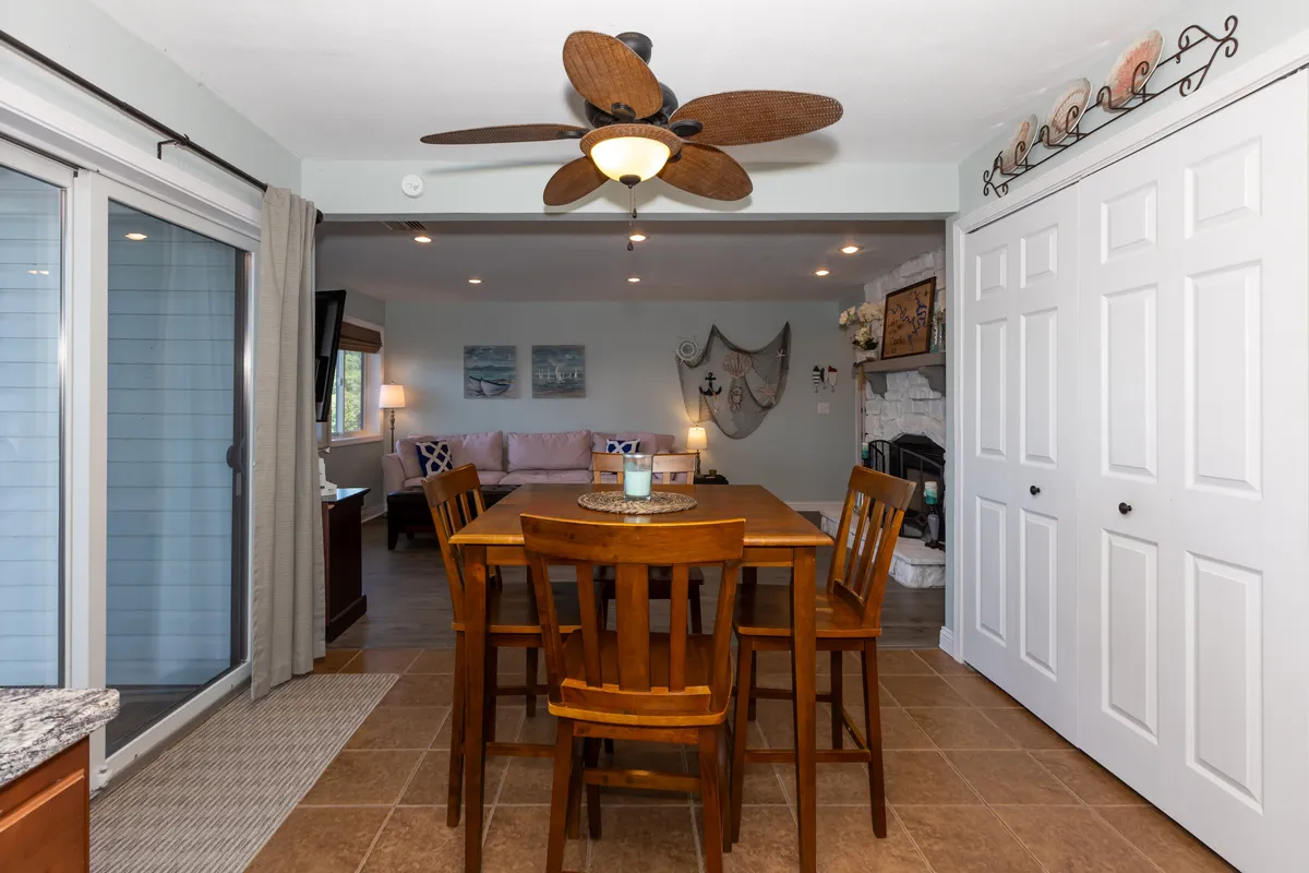 A welcoming dining and living space with a large table at its center, ceiling fan above, and cozy couch nearby. The décor is warm, and the open arrangement makes it ideal for shared meals, celebrations, or game nights.