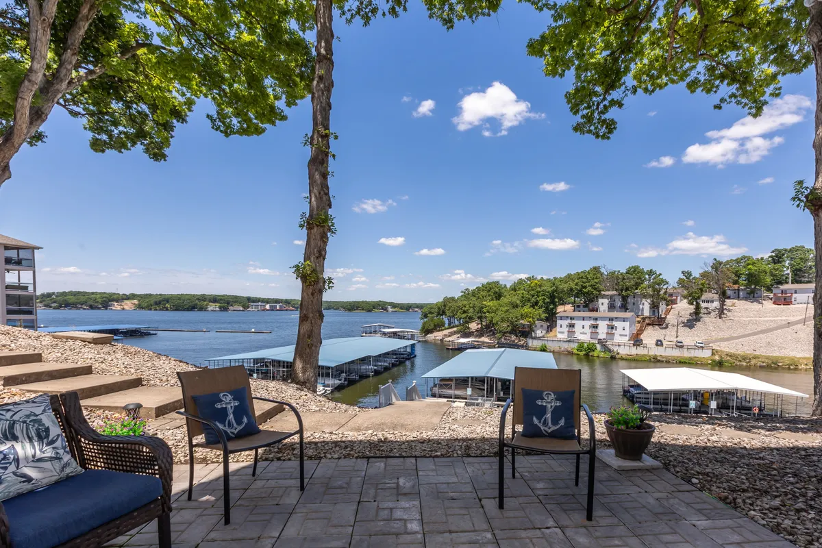 A tranquil outdoor seating area under a tree canopy overlooking a sweeping view of the lake. The patio is inviting for relaxing, reading, or enjoying nature, with scenic sunset views over the water.