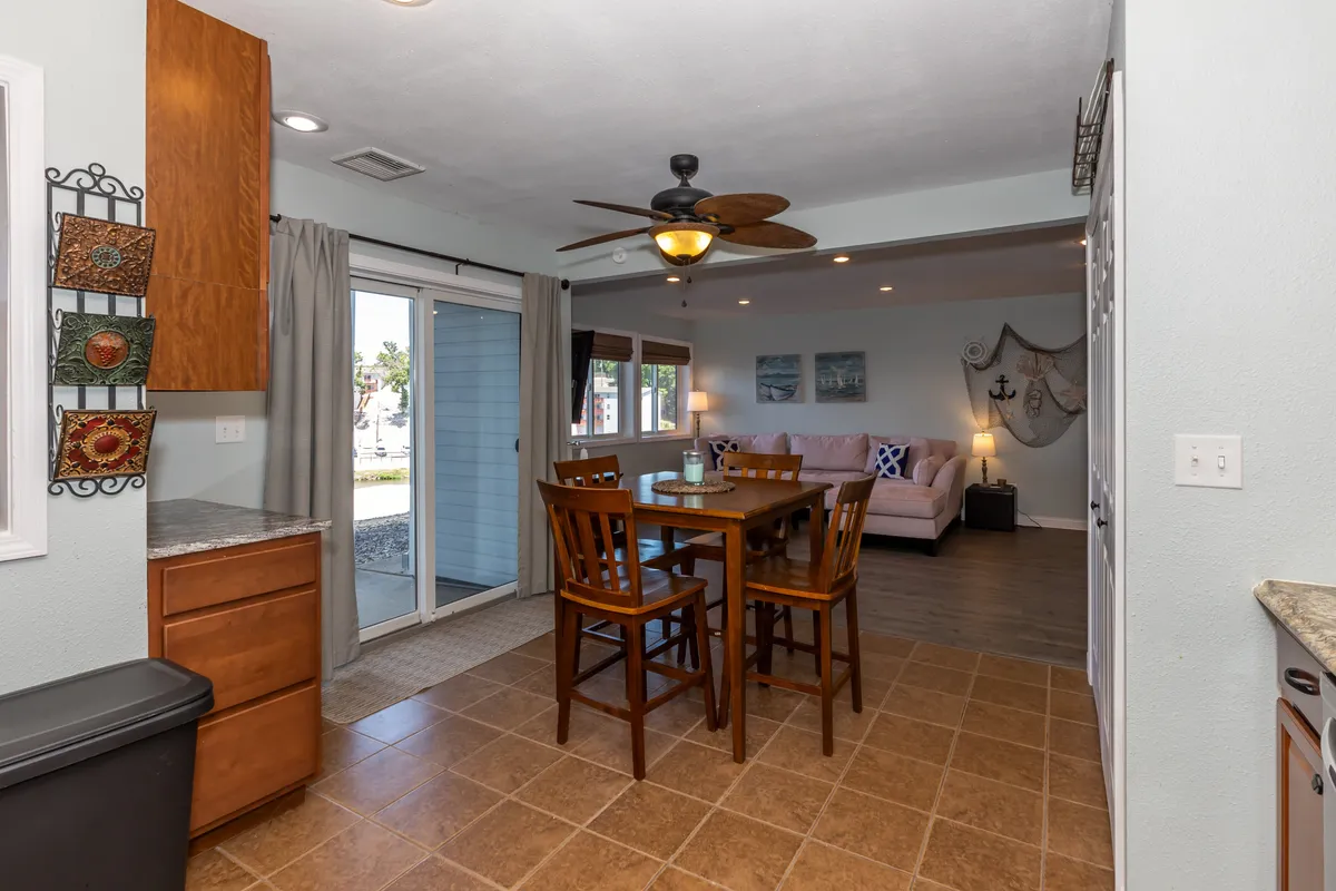 A sunlit dining area with a prominent dining table, adjacent to a sliding glass door that brings in natural light. The space blends the dining and living areas, showcasing versatility for family meals, games, and relaxed gatherings.