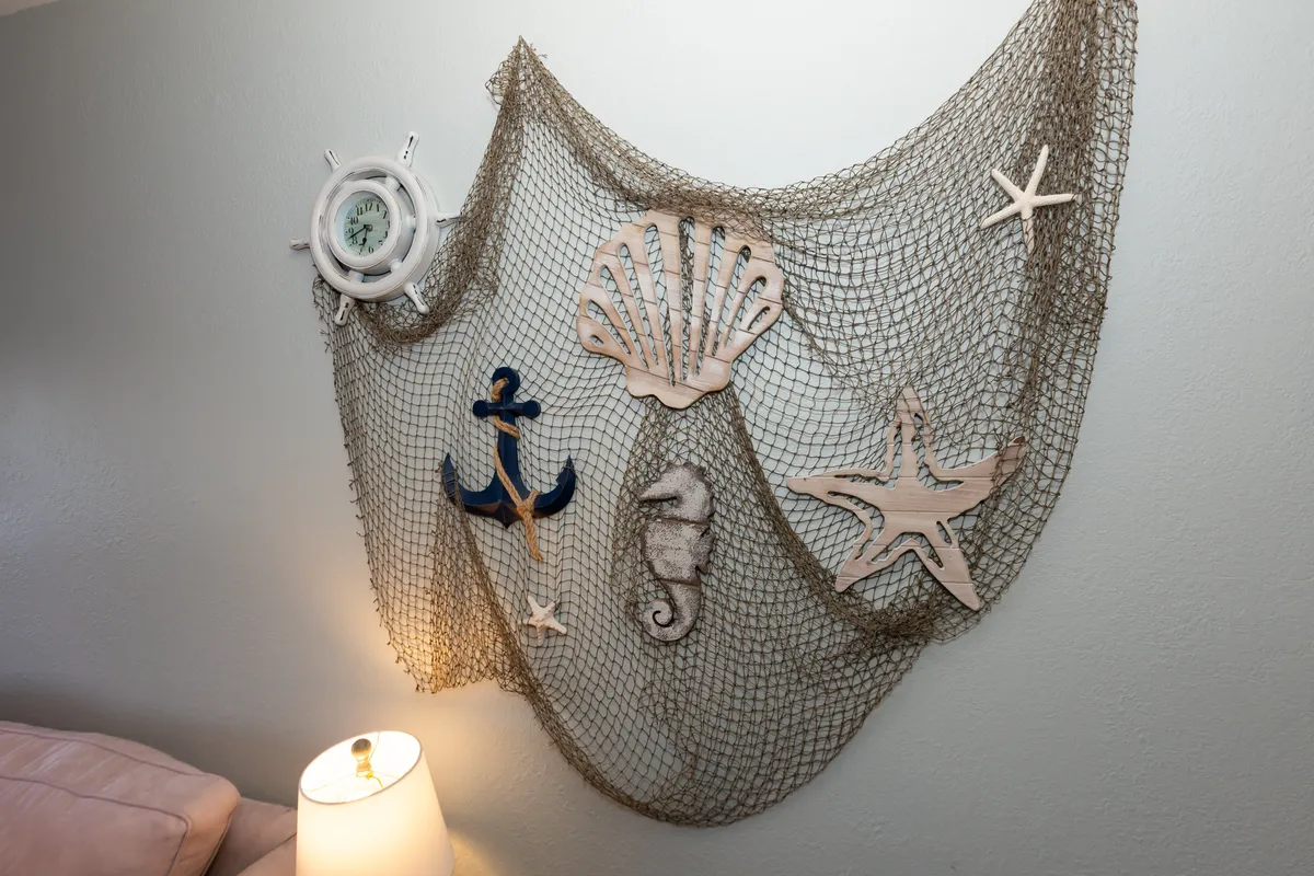 A cozy corner adorned with decorative fishing net, nautical clock, wooden anchor, seashells, seahorse, and starfish accents. The decor evokes maritime charm and the memory of beach and lake vacations, creating a relaxed and inviting environment for guests.