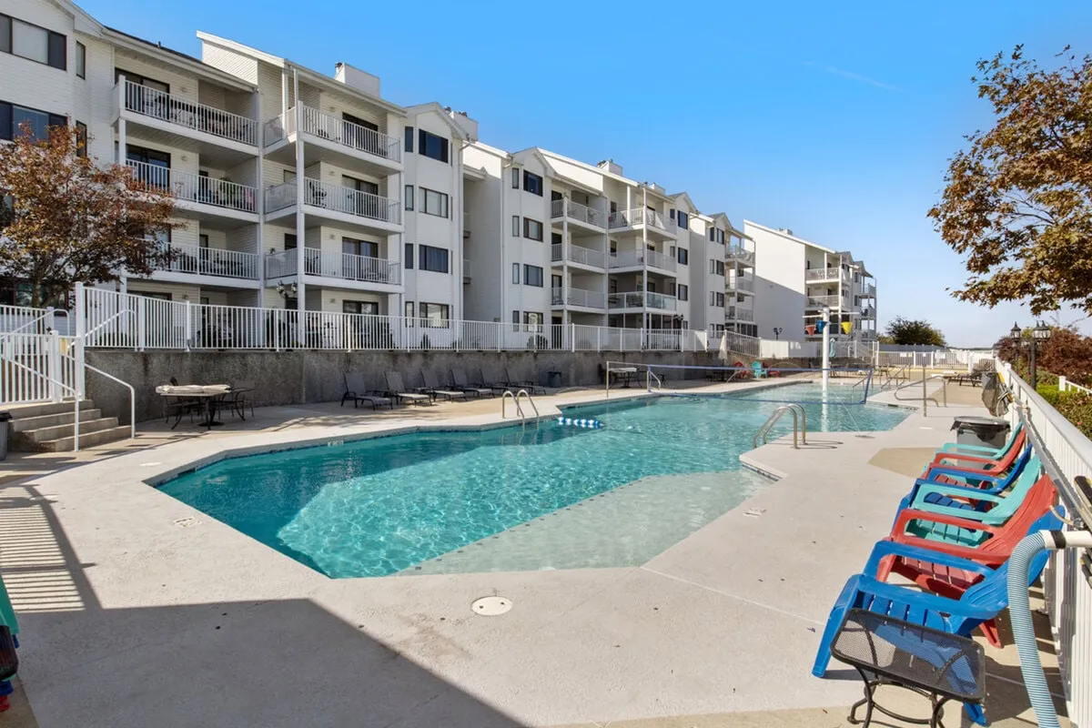 A relaxing pool area with inviting lounge chairs and a backdrop of surrounding apartments. The pool glistens under the sunlight, creating an atmosphere of leisure and luxury ideal for family swims or sun-soaked relaxation.