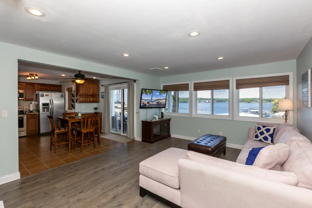 A welcoming open-concept living and dining area with plush seating, a dining table, a television, and expansive windows that offer stunning views of the lake. The space is filled with natural light, and the layout invites conversation and group gatherings.